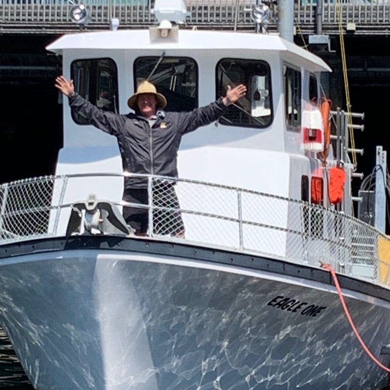 Person with arms raised standing on the deck of a boat named 'Eagle One' near a dock.