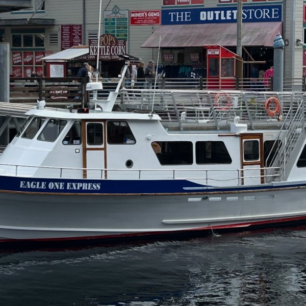 White passenger boat named Eagle One Express docked near shops on a cloudy day.