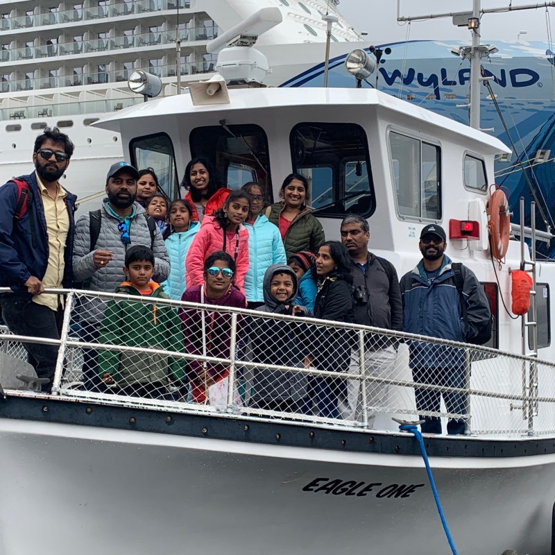 Group of people on the deck of a small boat named 'Eagle One', with a large cruise ship in the background.