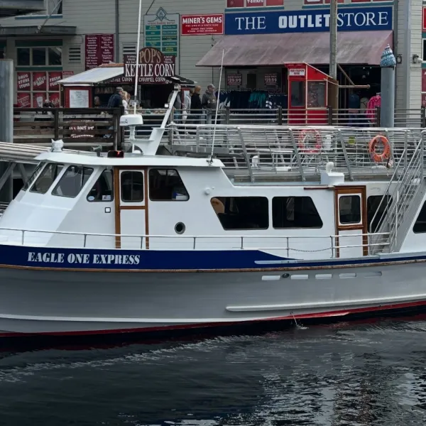 White boat 'Eagle One Express' docked by a boardwalk with shops in the background.
