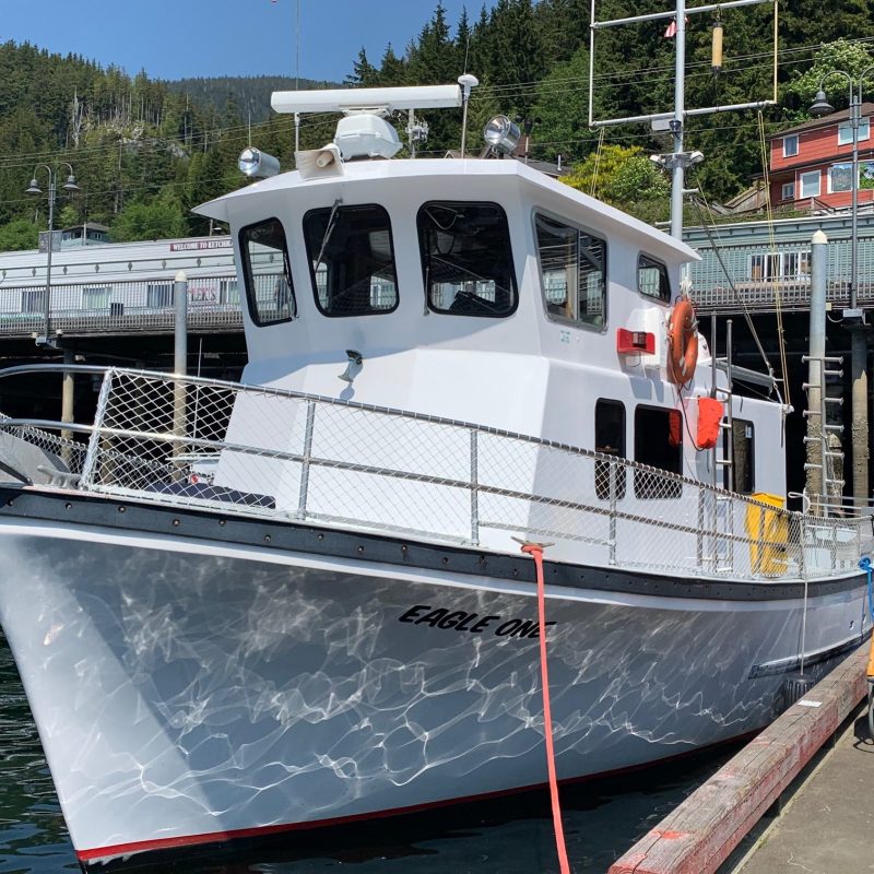 A white boat named 'Eagle One' docked at a marina with forested hills in the background.